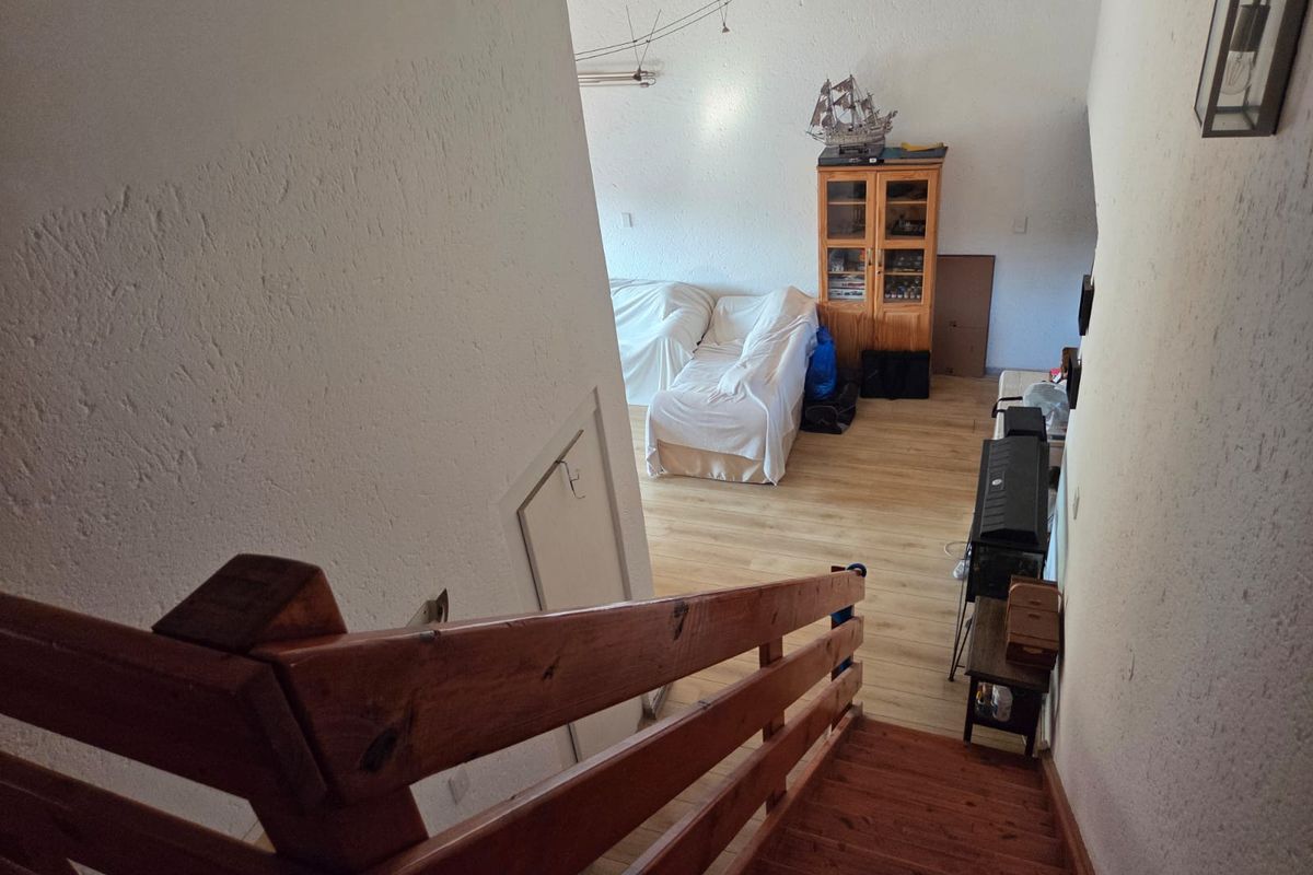 View looking down a wooden staircase into a living area featuring laminate flooring and textured wall finishes.