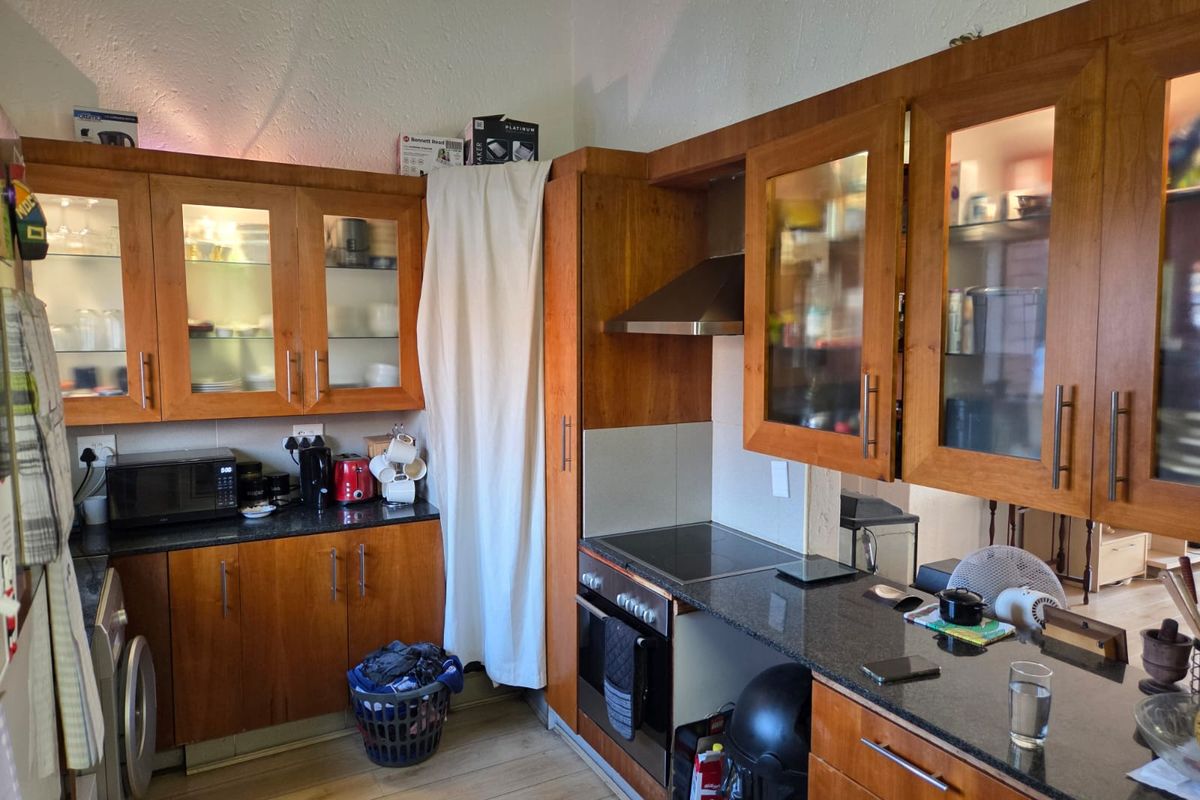 A functional kitchen featuring warm-toned wooden cabinetry, granite countertops, and integrated appliances including an oven, hob, and extractor fan.