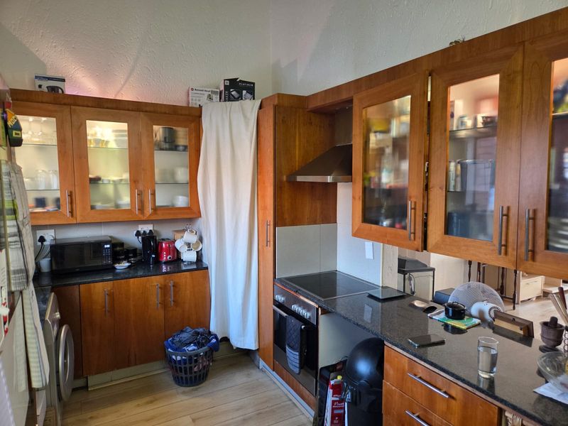 A functional kitchen featuring warm-toned wooden cabinetry, granite countertops, and integrated appliances including an oven, hob, and extractor fan.