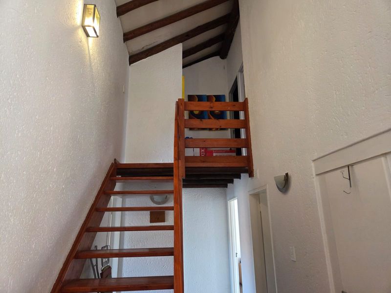 A bright hallway featuring a timber staircase leading to a mezzanine level with exposed wooden ceiling beams and textured white walls.