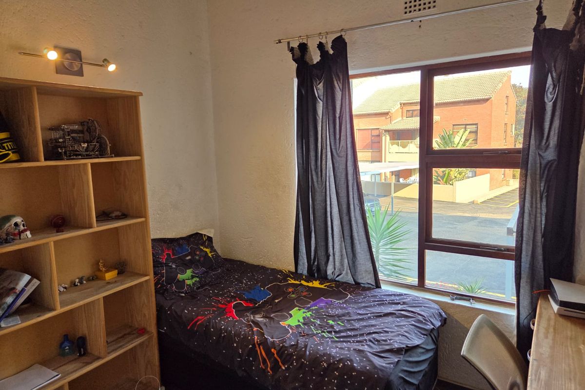 A standard bedroom featuring an aluminium-framed window with natural light and a built-in ventilation grille.