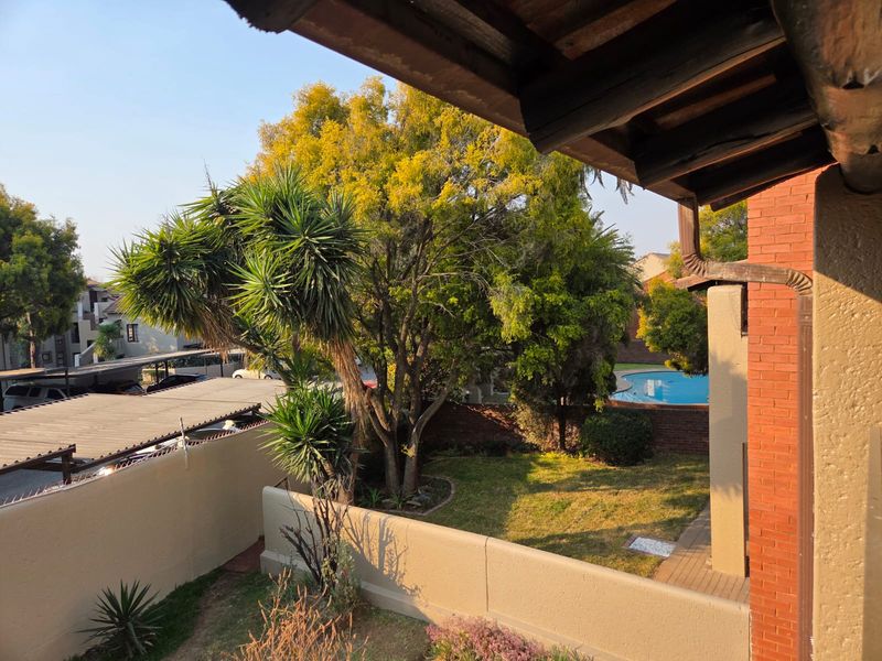 View from an elevated position overlooking a private garden, brick boundary wall, and a communal swimming pool area.