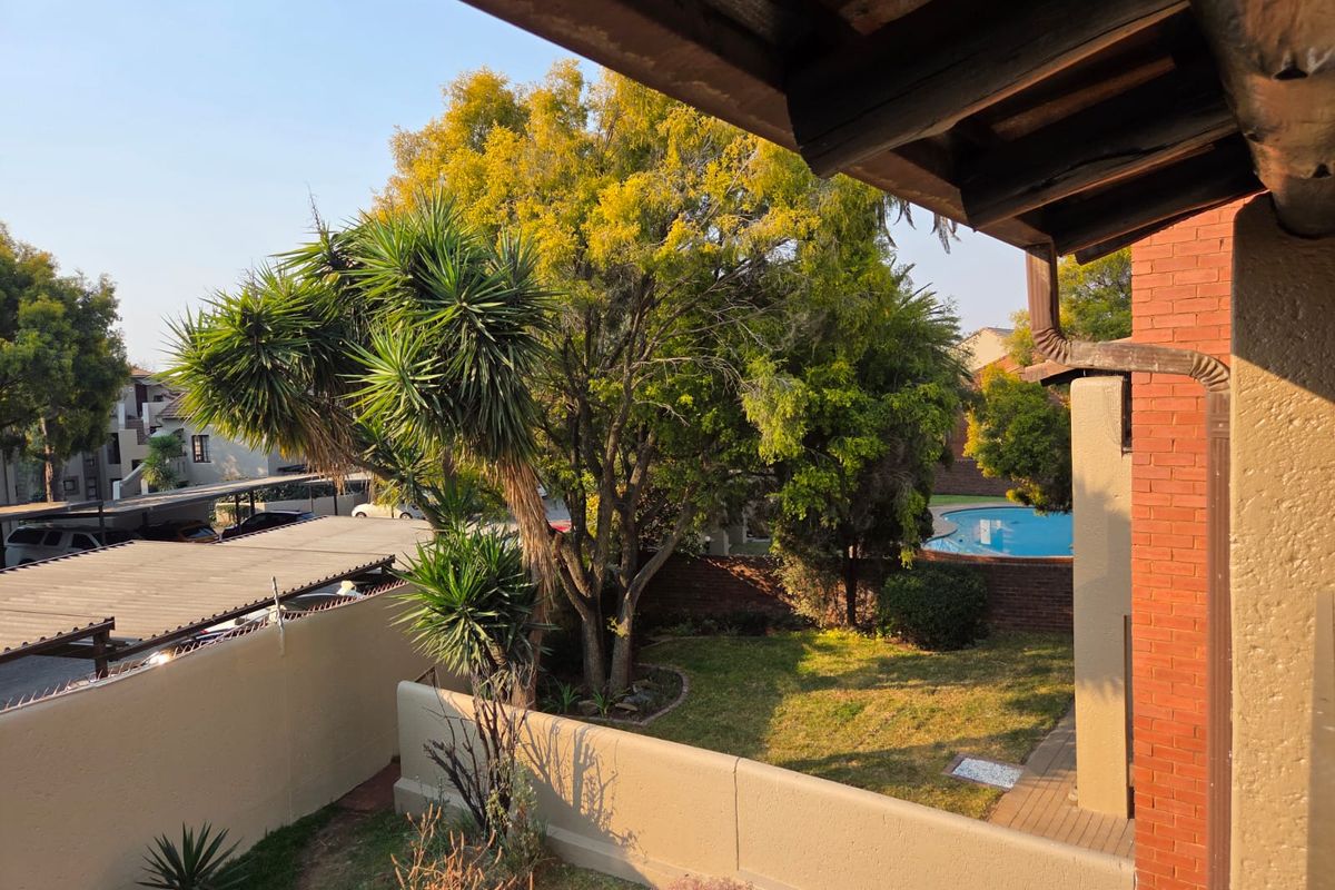 View from an elevated position overlooking a private garden, brick boundary wall, and a communal swimming pool area.