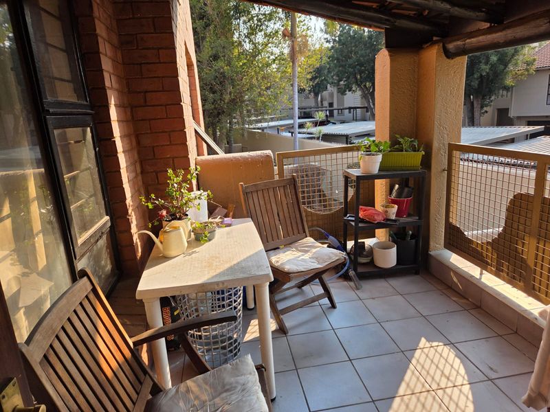 A covered balcony featuring tiled flooring, exposed brickwork, and a metal mesh balustrade, offering a functional outdoor space for relaxation.