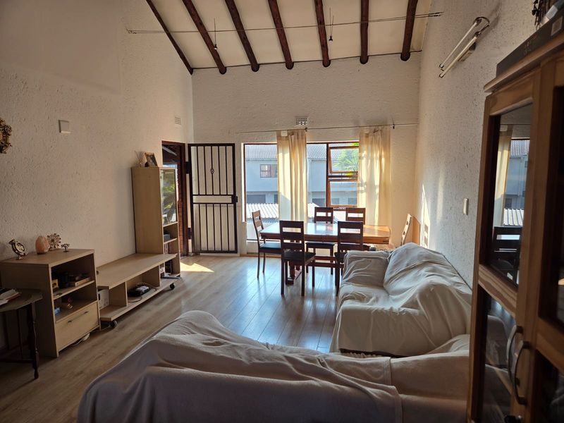 Spacious open-plan living and dining area featuring high ceilings with exposed timber beams, laminate flooring, and abundant natural light through large windows.