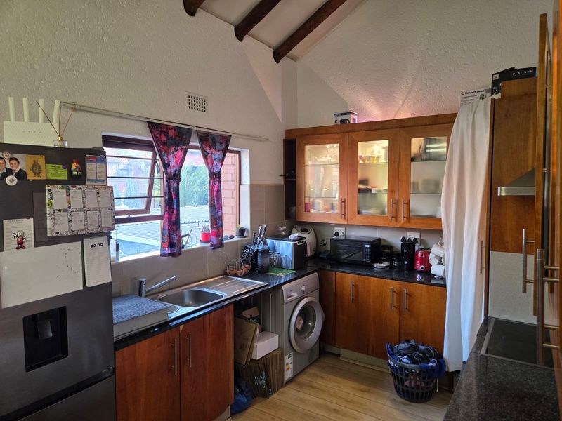 A functional kitchen featuring wooden cabinetry, granite countertops, a stainless steel sink, and exposed timber ceiling beams, providing a warm and practical workspace.