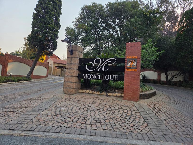 Entrance view of Monchique estate featuring a brick paved driveway and prominent stone and brick signage pillars.