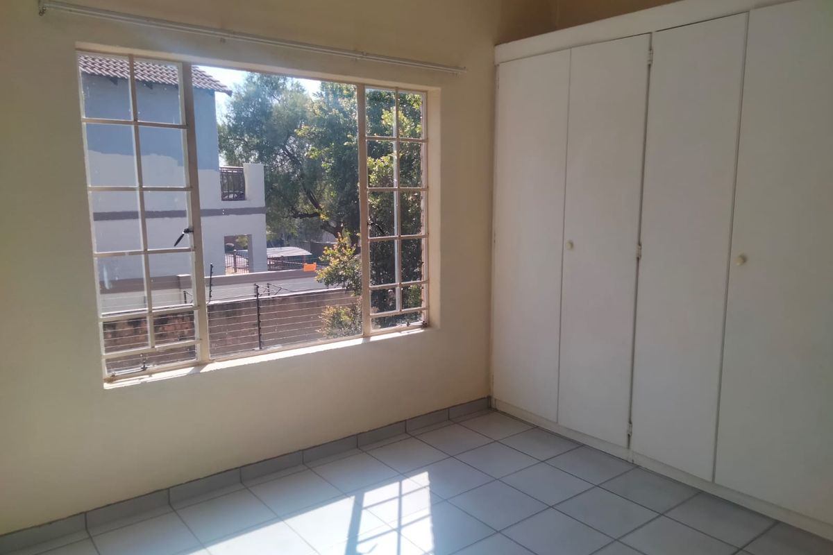 A bright, empty bedroom featuring tiled flooring and built-in cupboards, offering a clean and neutral space ready for personalization.