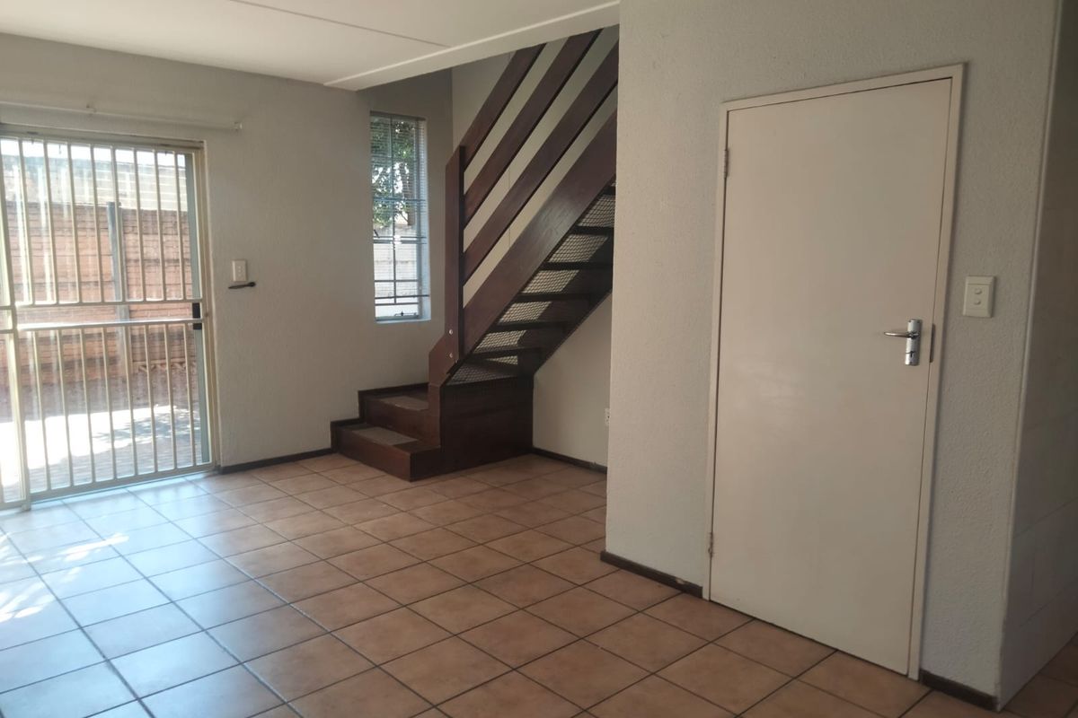 An empty living area featuring tiled flooring, a timber staircase, and a sliding door leading to the exterior.