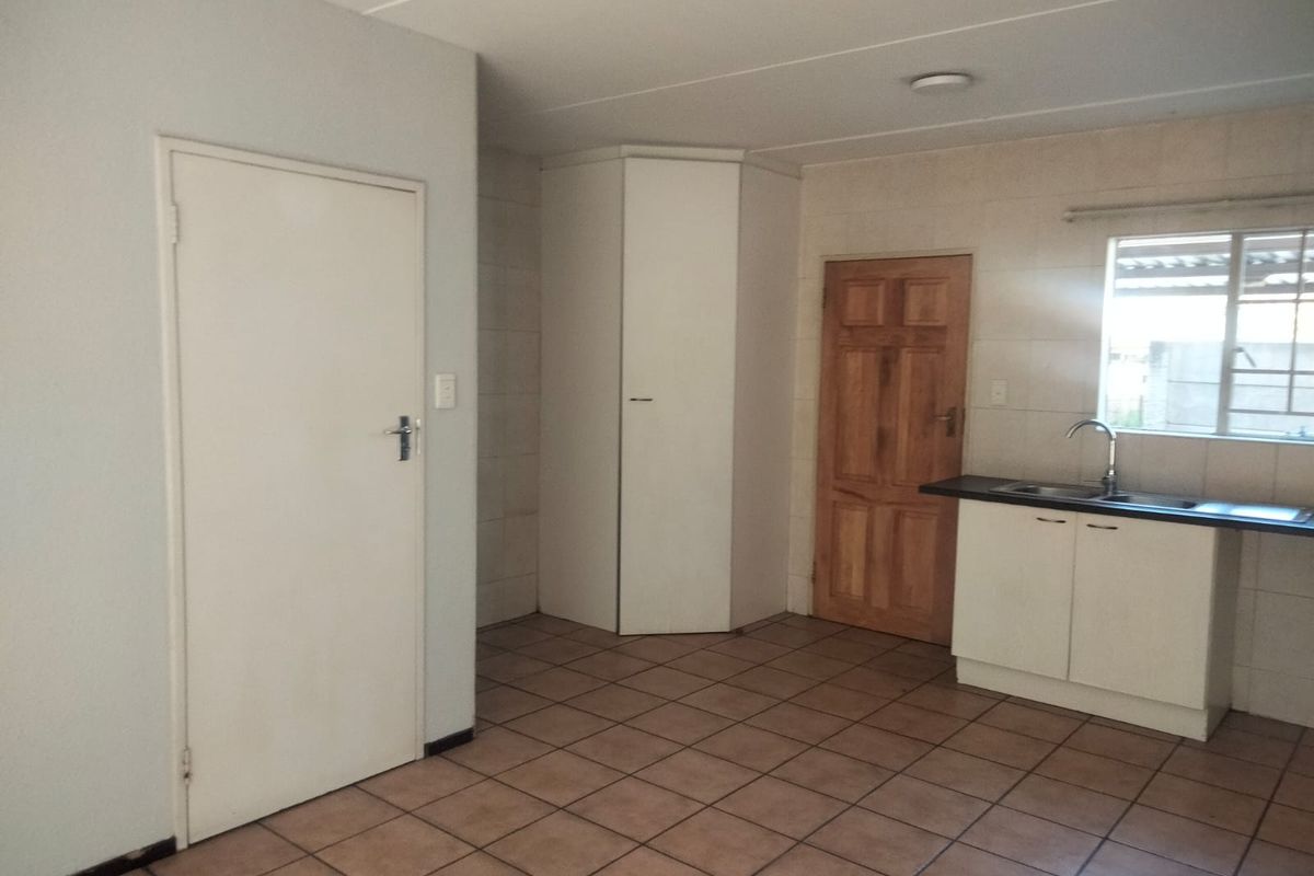 A functional kitchen area featuring tiled flooring, built-in cabinetry with a stainless steel sink, and a corner pantry cupboard.
