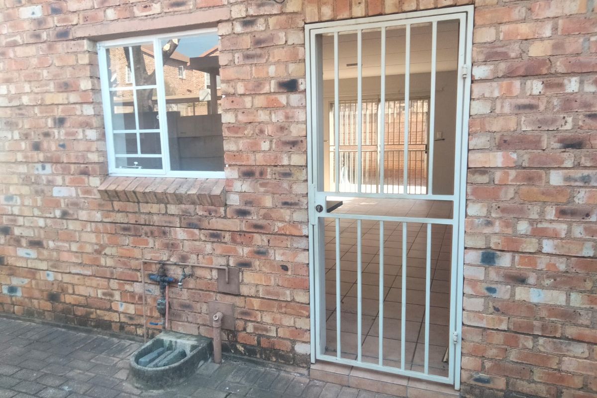 Rear exterior view of the townhouse featuring exposed brickwork, a secure metal gate, and a paved patio area with an external water connection.