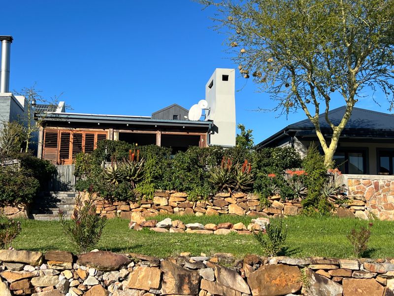 Rear view of the property featuring a landscaped garden with stone retaining walls, mature trees, and a covered patio area with timber shutters.