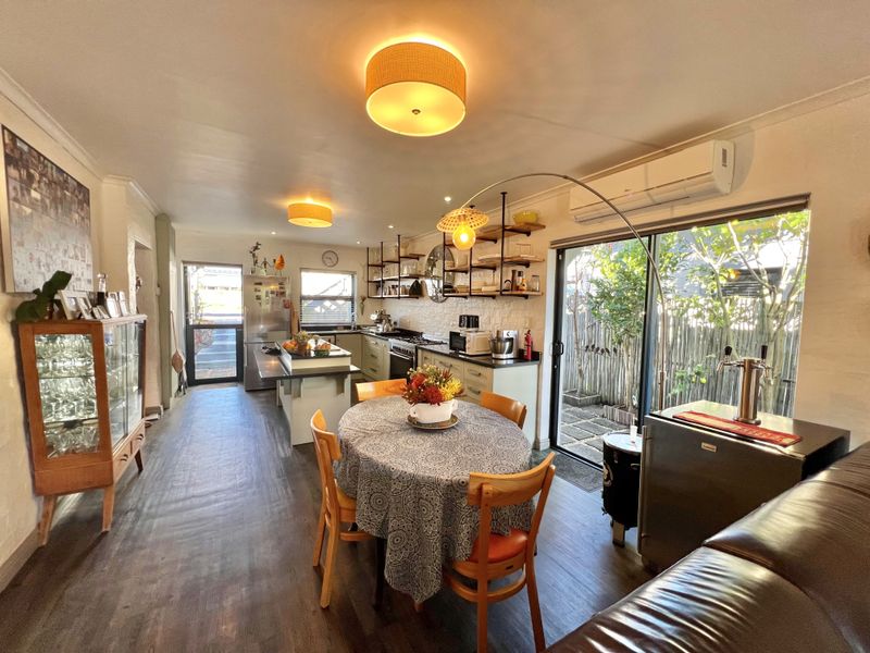 An open-plan living and kitchen area featuring modern cabinetry, open shelving, laminate flooring, and direct access to an outdoor patio through sliding glass doors.
