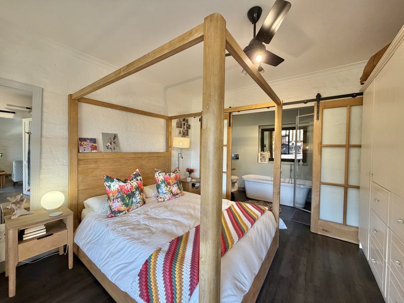 Spacious bedroom featuring a four-poster bed, dark laminate flooring, and an integrated en-suite bathroom with a freestanding bathtub and sliding barn door access.