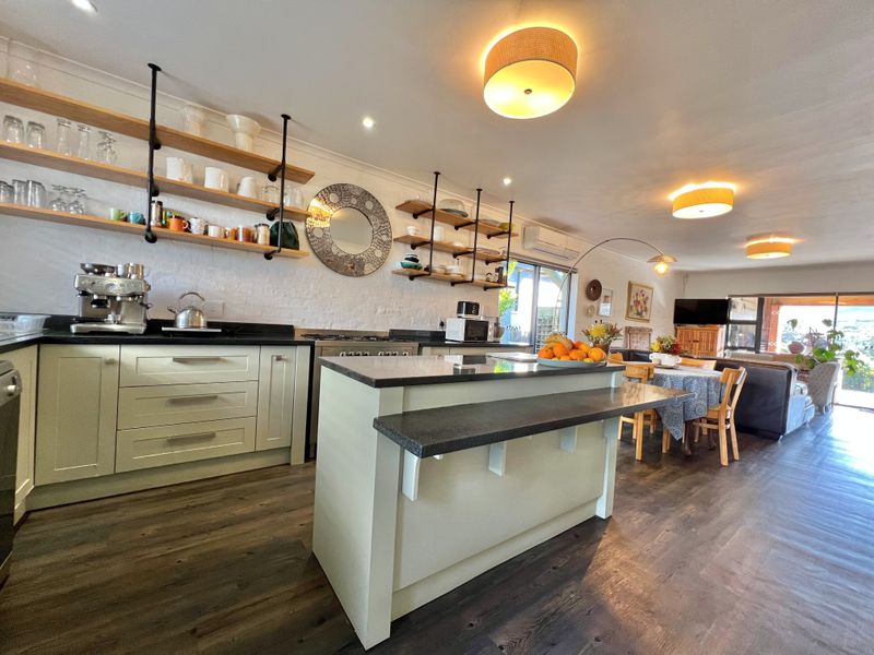 Spacious open-plan kitchen and living area featuring a central island, stone countertops, modern open shelving, and seamless flow to the outdoor patio.