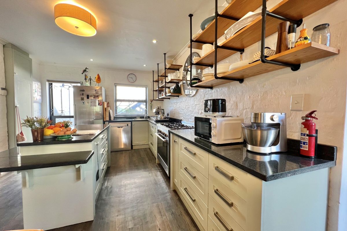 A well-appointed kitchen featuring granite countertops, gas hob, built-in cabinetry, and industrial-style open shelving, offering a functional and modern cooking space.