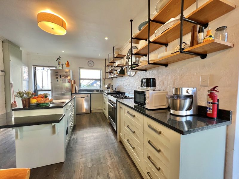 A well-appointed kitchen featuring granite countertops, gas hob, built-in cabinetry, and industrial-style open shelving, offering a functional and modern cooking space.
