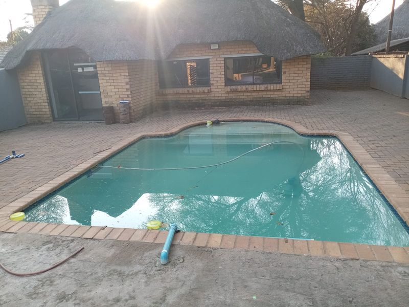 Outdoor pool area featuring a swimming pool with brick paving and a thatch-roofed brick structure in the background.