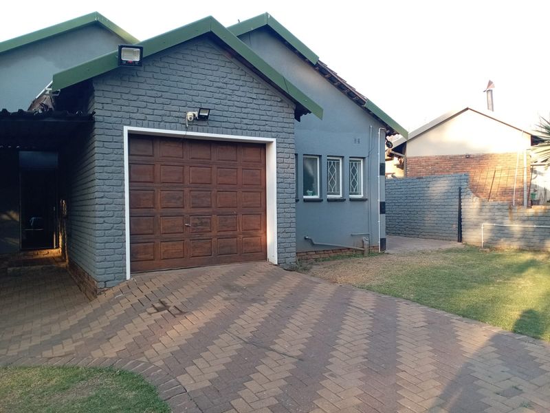 Front exterior view of the property featuring a paved driveway, single garage, and brick boundary wall with security lighting and camera installed.