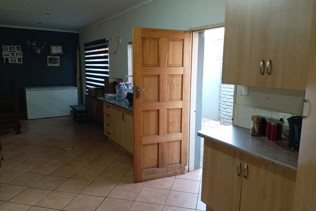 A functional kitchen area featuring built-in wooden cabinetry, laminate countertops, and tiled flooring, with direct access to an exterior space.