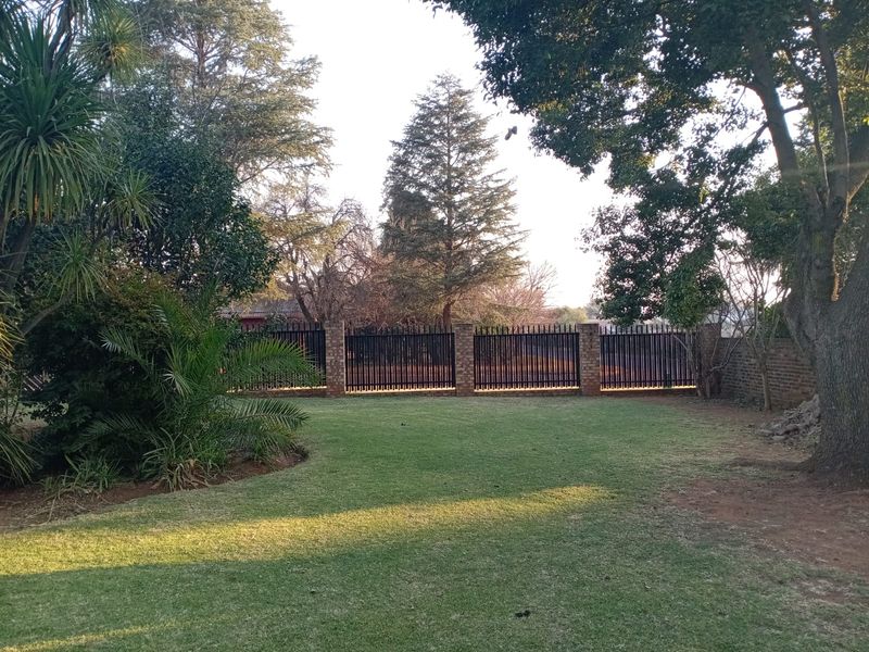 A well-maintained private garden featuring a lush lawn, mature trees, and secure brick and metal boundary fencing.