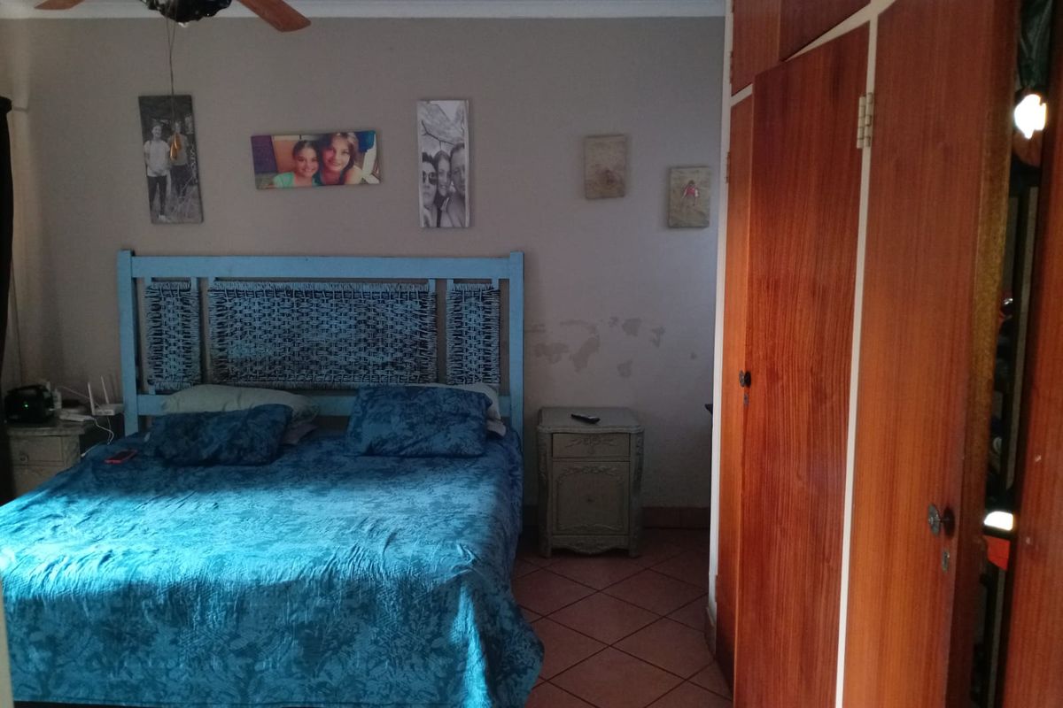 A bedroom featuring tiled flooring, a ceiling fan, and built-in wooden wardrobes, showing signs of wear on the wall finish.