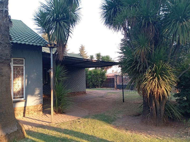 Front exterior view of the house featuring a paved driveway, carport, and established garden with mature trees.