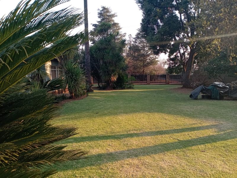 A spacious, well-maintained garden featuring a large lawn, mature trees, and secure perimeter fencing.