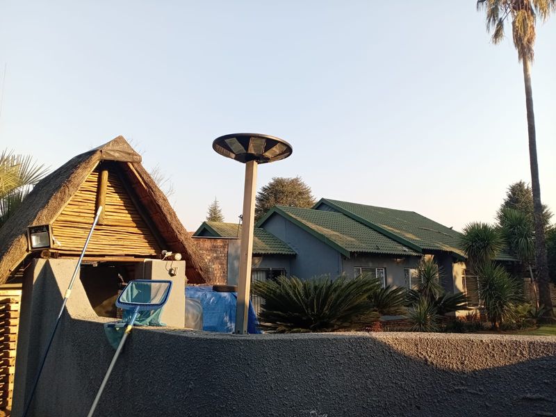 Rear view of the property featuring a thatched outdoor structure, tiled roof main house, and established garden with boundary walling.