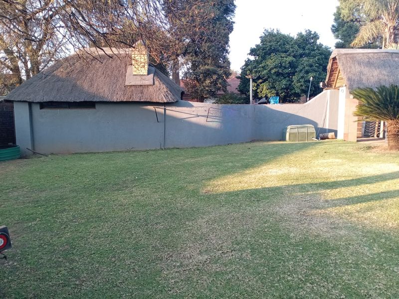 A spacious backyard garden featuring a well-maintained lawn and a structure with a traditional thatch roof and brick chimney.