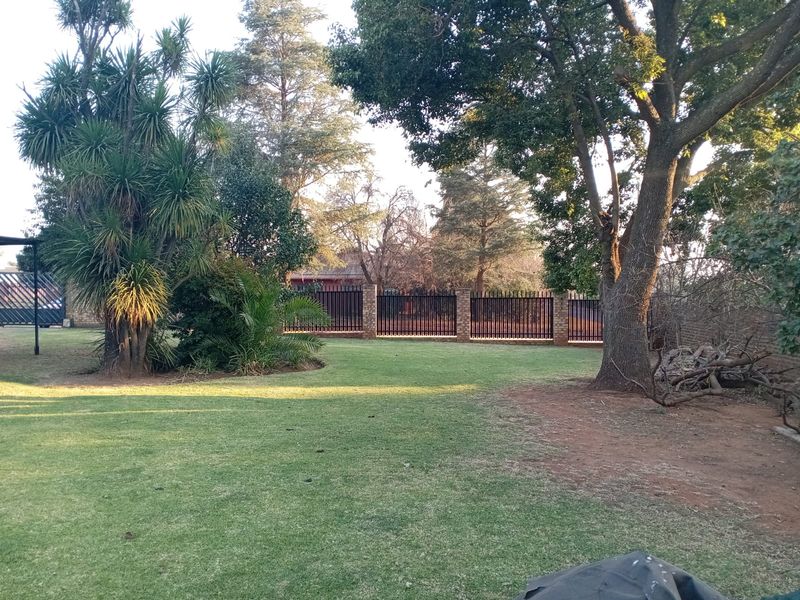 A spacious private garden featuring a well-maintained lawn, mature trees, and secure brick and steel perimeter fencing.