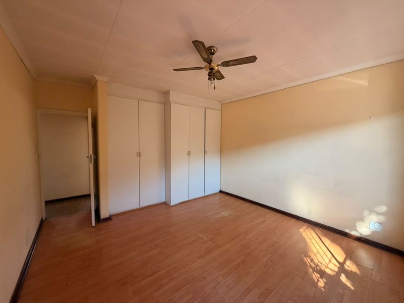 An empty bedroom featuring laminate flooring, built-in cupboards, and a ceiling fan, ready for a fresh coat of paint and new styling.