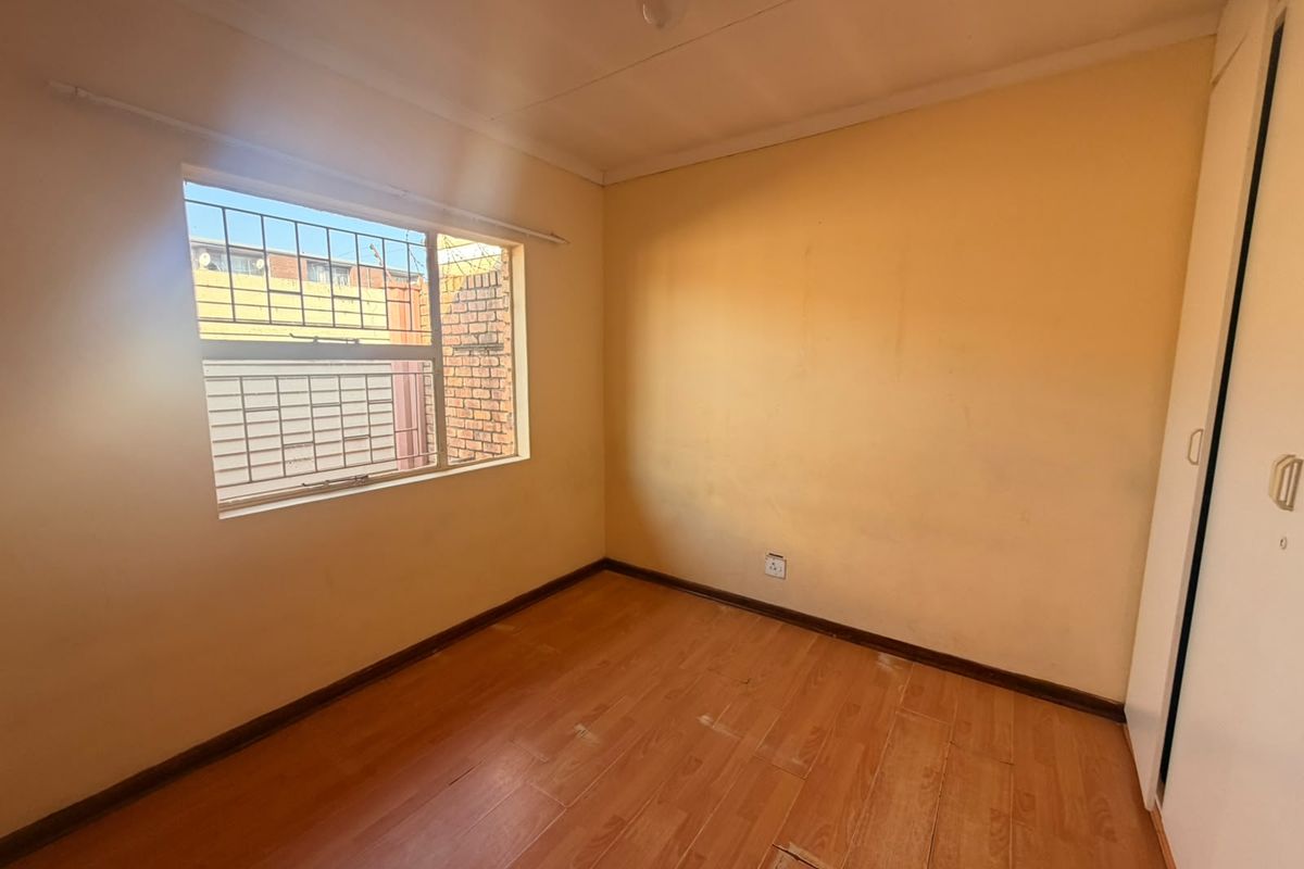 An empty bedroom featuring laminate flooring, a built-in wardrobe, and security bars on the window. The room requires cosmetic updates to walls and flooring.
