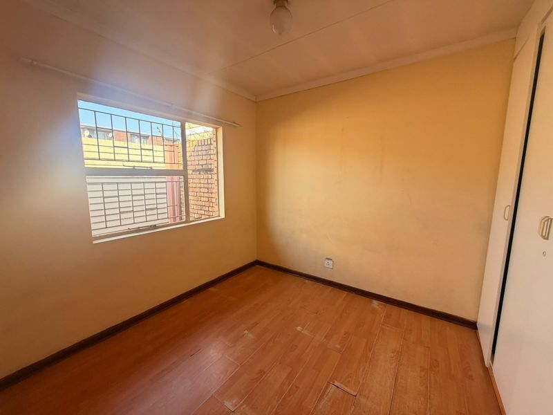 An empty bedroom featuring laminate flooring, a built-in wardrobe, and security bars on the window. The room requires cosmetic updates to walls and flooring.