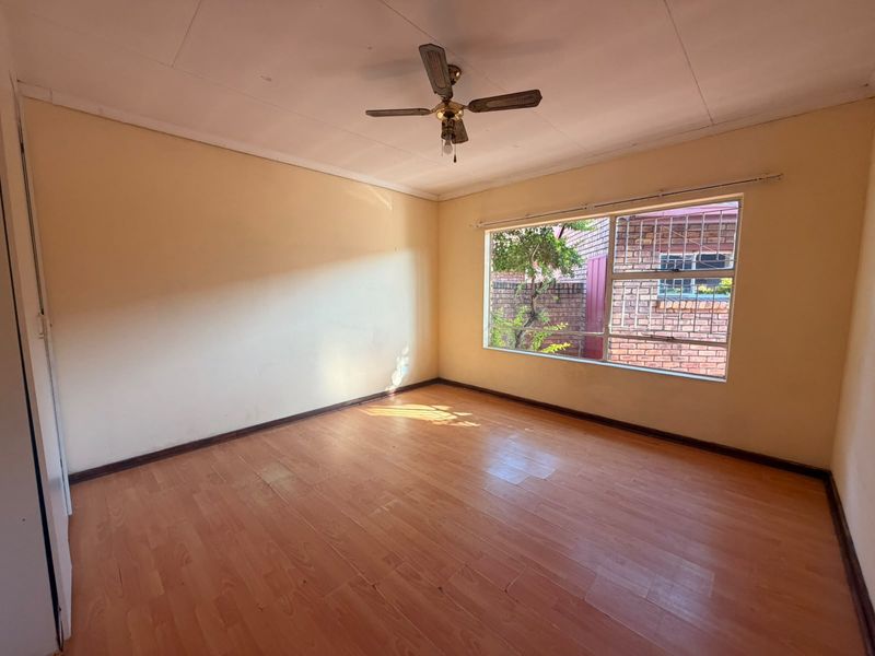 An empty bedroom featuring laminate flooring, a ceiling fan, and a window with security bars, offering a blank canvas for personalization.