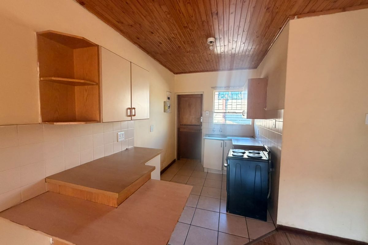 A functional kitchen featuring wooden ceilings, tiled flooring, built-in cabinetry, and a tiled backsplash, offering a blank canvas for modern renovation.