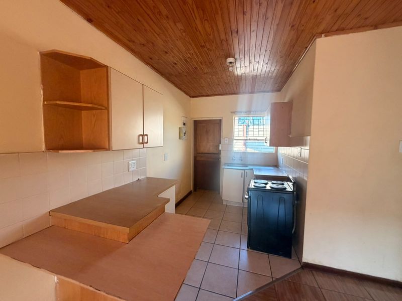 A functional kitchen featuring wooden ceilings, tiled flooring, built-in cabinetry, and a tiled backsplash, offering a blank canvas for modern renovation.