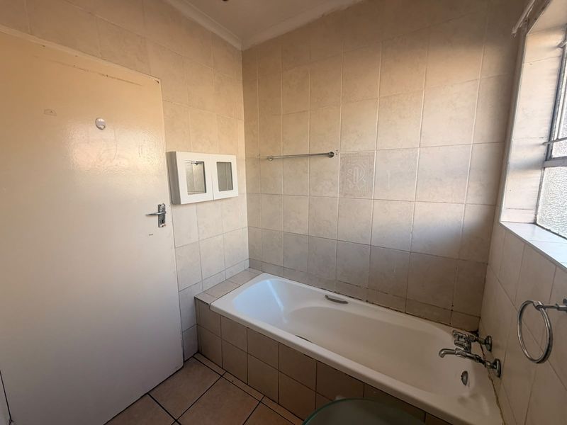 A dated bathroom featuring a built-in bathtub, tiled walls and flooring, and a wall-mounted medicine cabinet, offering potential for modernization.