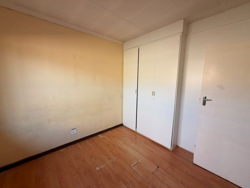 An empty bedroom featuring laminate flooring and a built-in wardrobe, requiring cosmetic updates to the walls and flooring.