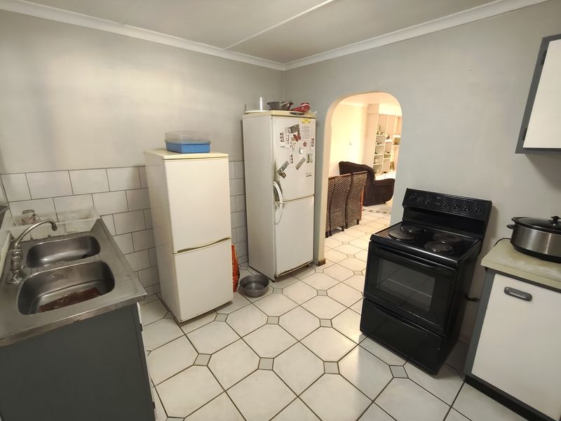 A functional kitchen featuring a double stainless steel sink, tiled splashback, and a freestanding electric stove, with direct access to the adjacent living area.