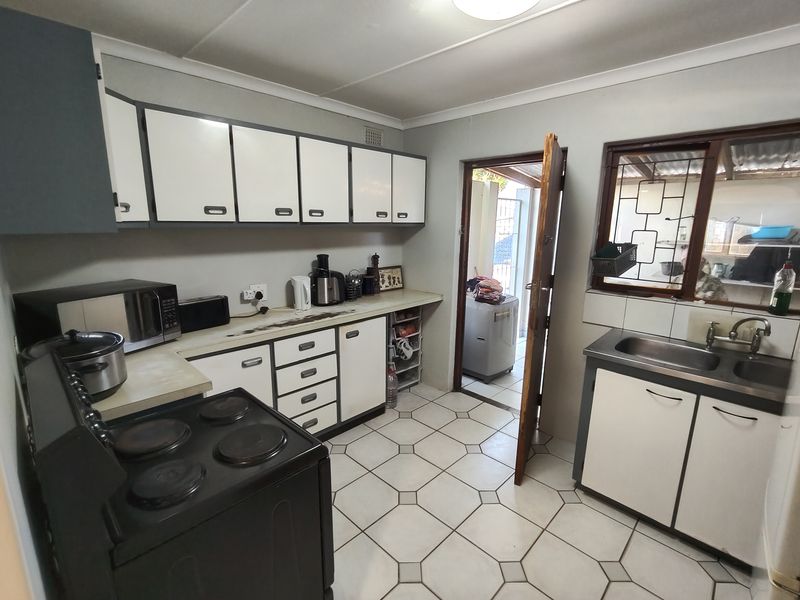 A functional kitchen featuring white cabinetry, laminate countertops, a stainless steel sink, and tiled flooring, providing a practical workspace with direct access to the rear.
