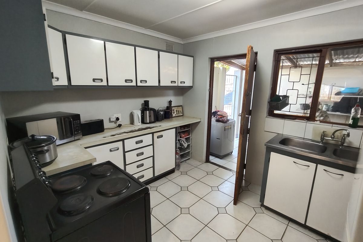 A functional kitchen featuring white cabinetry, laminate countertops, a stainless steel sink, and tiled flooring, providing a practical workspace with direct access to the rear.