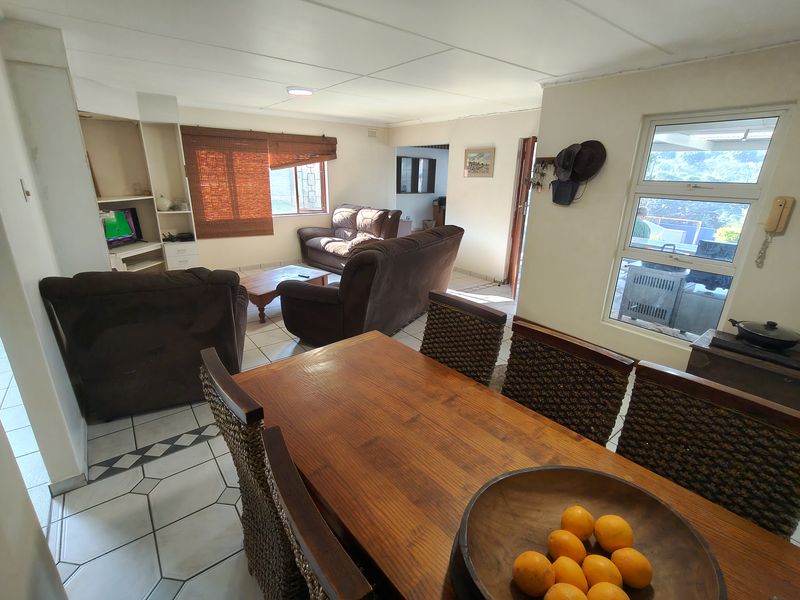 Open-plan living and dining area featuring tiled flooring, built-in shelving, and large windows providing natural light and access to the outdoor space.