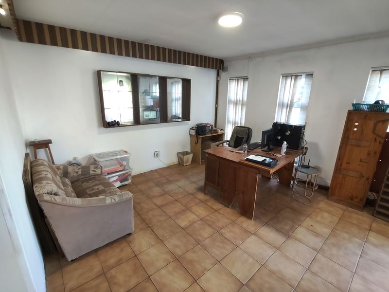 A functional office space featuring tiled flooring, built-in wall cabinetry, and vertical window blinds, offering a practical layout for a home workspace.