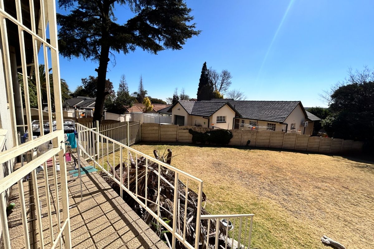 A view of the rear garden and patio area featuring a concrete terrace with metal security railings and a large lawn.