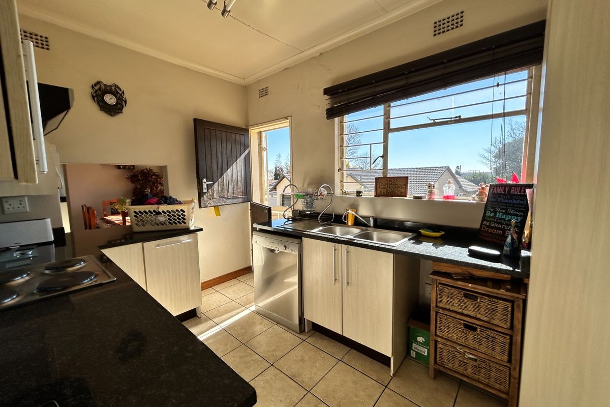 A functional kitchen featuring dark countertops, built-in cabinetry, a double sink, and tiled flooring with direct access to the exterior.