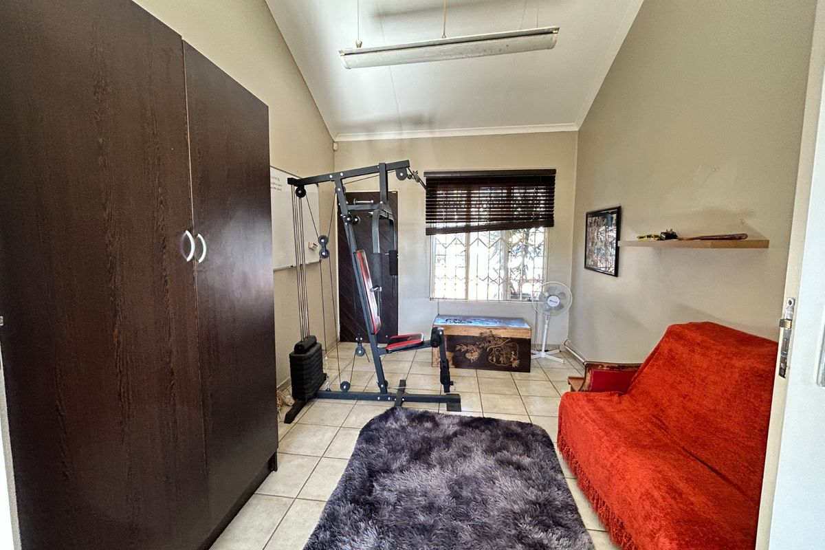 A bedroom featuring tiled flooring, a built-in wardrobe, and a vaulted ceiling with security bars on the window.
