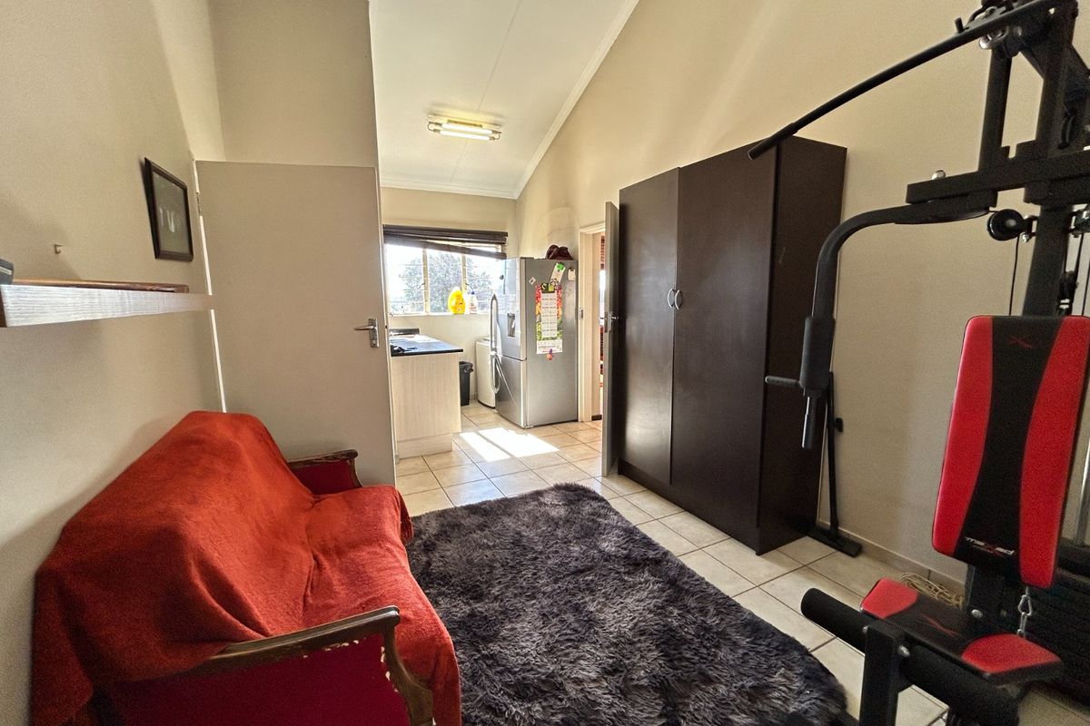 A multi-purpose living area featuring tiled flooring and a vaulted ceiling, with an adjacent view into the kitchen area.
