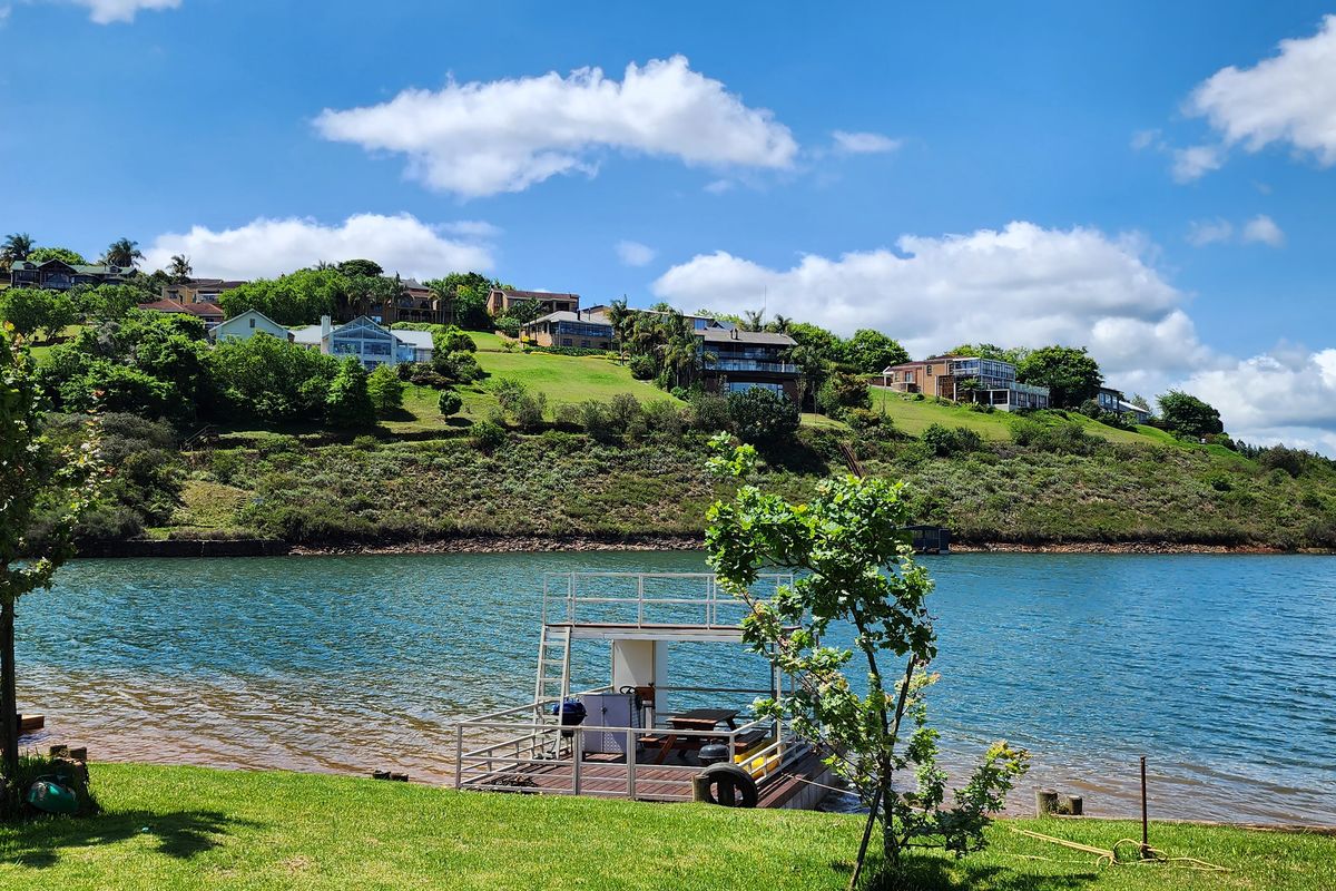 Scenic waterfront view featuring a private floating jetty and well-maintained lawn, overlooking a tranquil lake with hillside residential properties in the background.
