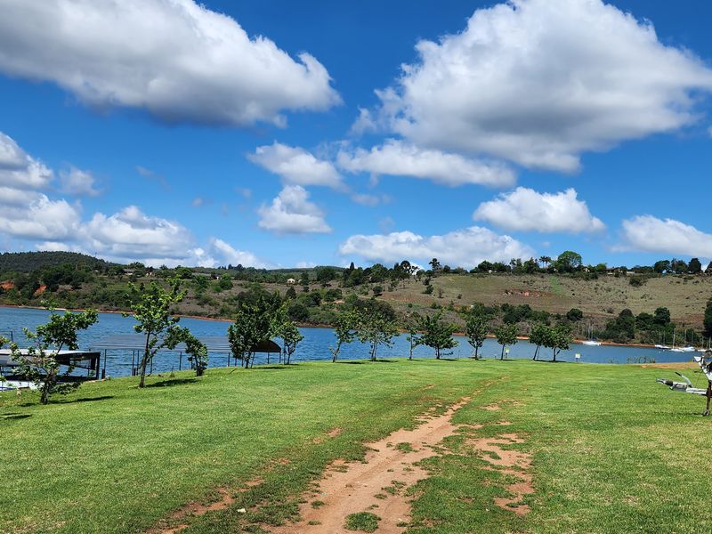 A scenic view of the waterfront property featuring a well-maintained lawn, mature trees, and direct access to the lake.